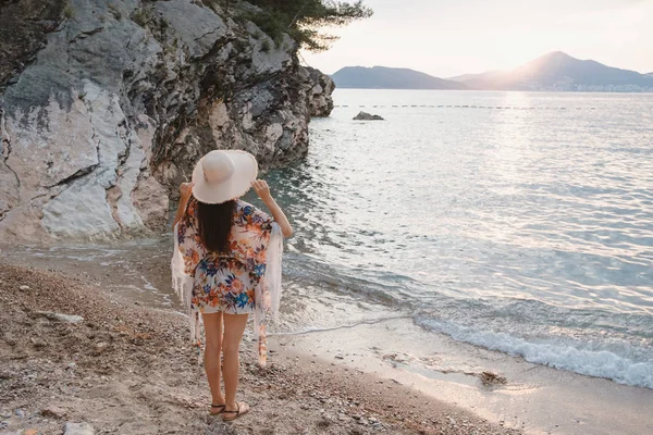 一个年轻美丽的女人在海滩上抱着她的草帽的背面视图 并期待地平线 — 图库照片