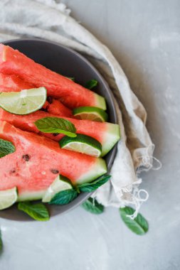 Karpuz dilimleri ve kireç bir plaka üzerinde gri bir arka plan üzerinde