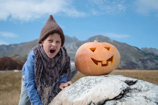 自然の背景に帽子と彫られたカボチャのハロウィーンのかわいい男の子 — ストック写真