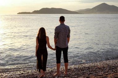 Bir erkek ve bir kadın batan güneşin zemin karşı deniz kenarında oturan siyah elbiseli arkasında. Bir tarihte romantik çift