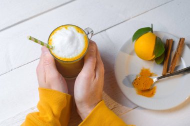 Adam elleriyle zerdeçal latte veya gözlük zencefil ve limon beyaz bir tablo ile altın süt