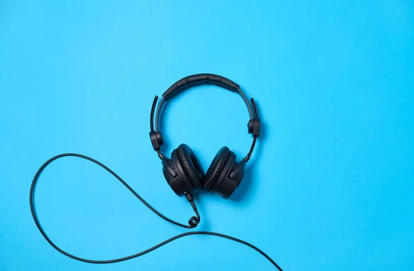 Música o podcast de fondo con auriculares en la mesa azul, plana — Foto de Stock