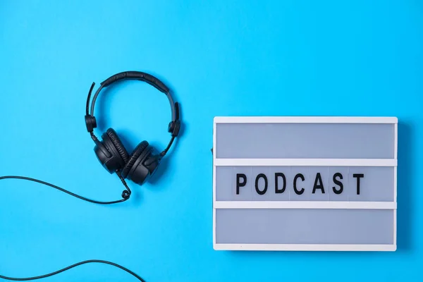 Bakgrund med hörlurar och Podcast ordet på ljusbord på blå — Stockfoto