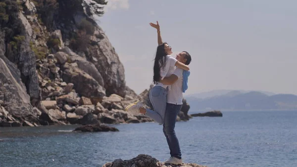 Esposo y esposa se abrazan y se paran en una roca cerca del mar en — Foto de Stock