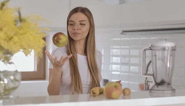 Ung blond kvinna i vit t-shirt förbereder frukt smoothie i bl — Stockfoto