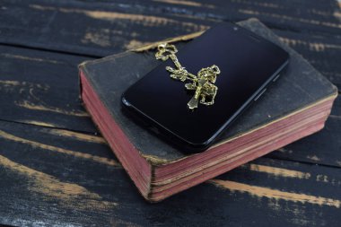 Altın haç, cep telefonu ve masanın üzerine antik kutsal İncil