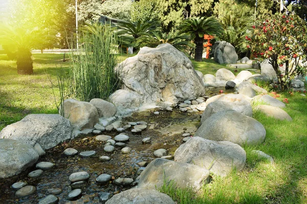 a mountain spring of water flows from the mountain to the stones on the green lawn on a warm summer day