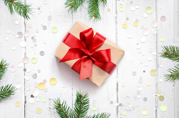 Подарочная коробка с красной лентой на деревянном фоне с сосновыми ветвями. Вид сверху
.