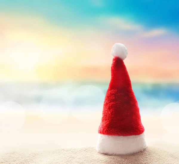 Santa Claus hat on white sand of tropical beach. Christmas or New Years vacation concept. — Stock Photo, Image