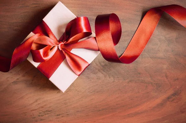 White gift box and red ribbon with tag on wood background. Vintage gift box on wooden board with space for text.