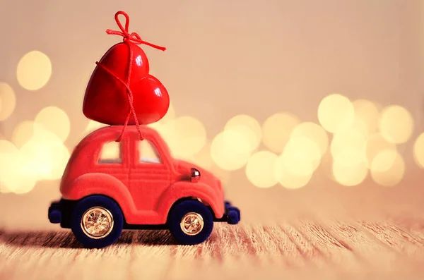 Little red beetle car carries a red heart. The concept of Valentine Day.