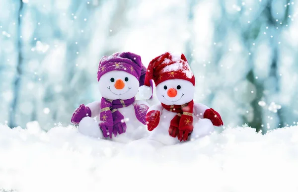 Twee kleine sneeuwpoppen het meisje en de jongen in caps en sjaals op sneeuw in de winter. Achtergrond met een grappige sneeuwpop. Kerstkaart. — Stockfoto