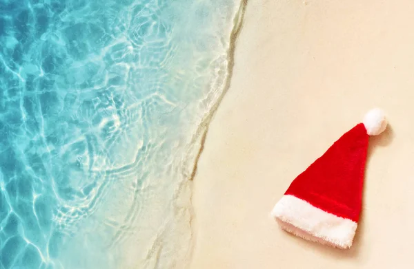 Christmas holidays concept. Top view of santa claus hat on summer sand beach. — Stock Photo, Image