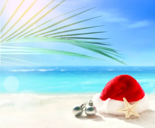 Christmas holidays concept. Santa claus hat and starfish on summer sand beach. — Stock Photo, Image
