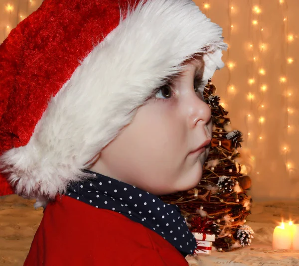 サンタ クロースの赤い帽子の小さな赤ちゃんは クリスマスを祝います 赤キャップで幼児のクリスマスの写真です 新年の休日とクリスマス ツリー — ストック写真