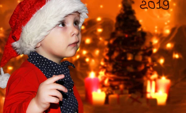 サンタ クロースの赤い帽子の小さな赤ちゃんは クリスマスを祝います 赤キャップで幼児のクリスマスの写真です 新年の休日とクリスマス ツリー — ストック写真