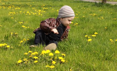 Güzel bir bebek çocuk mutlu portre gülümseyerek, karahindiba parkta blooming taze yeşil çimenlerin üzerinde oturan