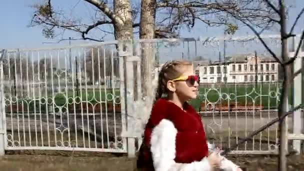 Маленька дівчинка в сонцезахисних окулярах приходить і полегшує собі телефон селфі — стокове відео