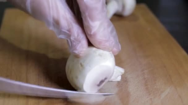 Tangan wanita dalam sarung tangan transparan memotong jamur di papan kayu dengan pisau putih — Stok Video