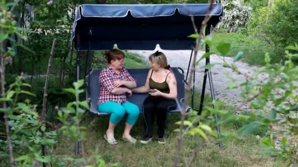 Dos Mujeres Están Sentadas Columpio Jardín Hablando Entre — Vídeo de stock