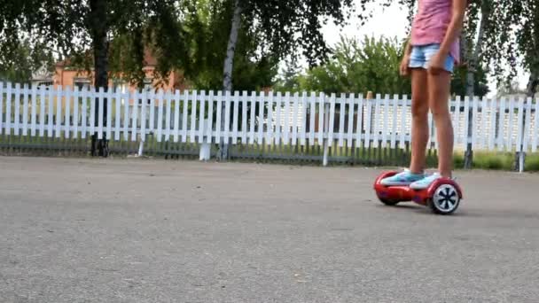 Meisje rijdt een gyroboard op de stoep van een omheind asfalt — Stockvideo