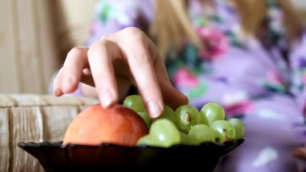 La mano de una niña en un vestido púrpura con un estampado brillante toma una uva de un plato — Vídeo de stock