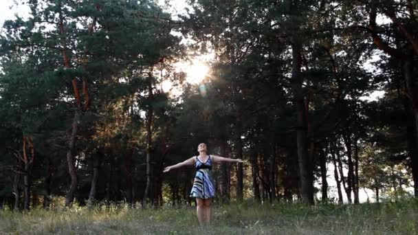 Mujer en un vestido colorido realiza ejercicios de respiración profunda entre los pinos altos en un día soleado — Vídeo de stock