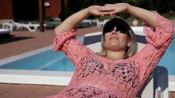 Blondine, die mit beiden Händen auf einem Liegestuhl liegt, verbirgt ihr Gesicht vor der Sonne — Stockvideo