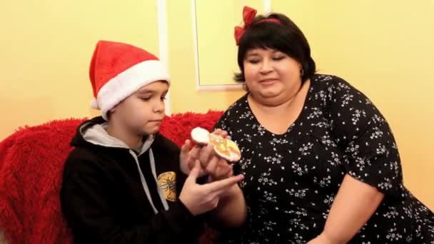 胖胖的妈妈和儿子在圣诞老人的帽子正在看彩绘姜饼 — 图库视频影像