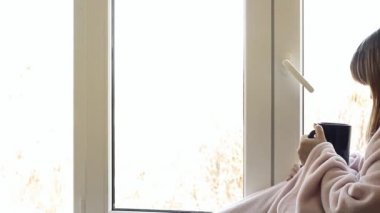 pencerenin kenarında büyük bir mavi fincan sıcak çay içme sıcak pembe bornoz içinde tek kadın