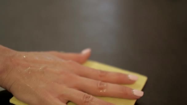 La mano bagnata femminile sfrega un tavolo scuro con uno straccio giallo — Video Stock