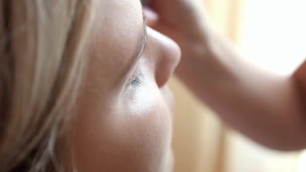 Make-up artiest voert een brede borstel gezicht meisje van Europese verschijning, zeer nauwe plan — Stockvideo