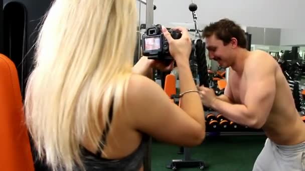Девушка фотограф снимает спортсмена, который выполняет упражнения на тренажере — стоковое видео