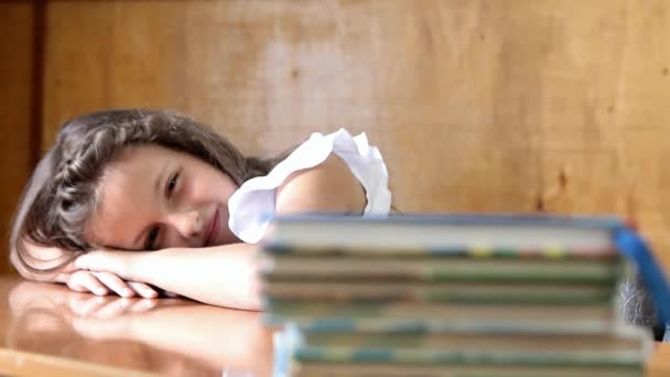 机の上に横たわる小さな女の子 本の山を見た — ストック動画
