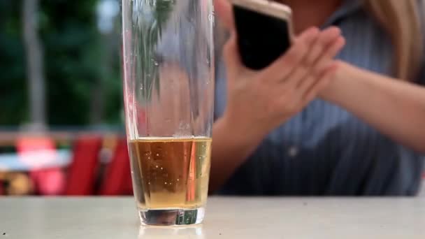 Sur le fond d'une boisson gazeuse dans un verre transparent, les mains féminines tordent le téléphone — Video