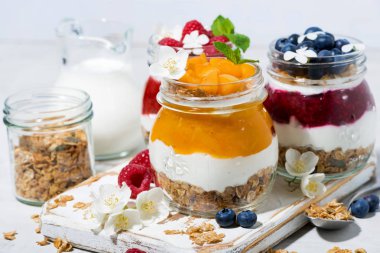 Beyaz ahşap tahta, closeup yatay olarak kavanozlara tatlılar granola, berry ve meyve püresi