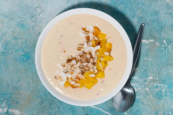 smoothie bowl with mango, coconut and nuts, top view closeup