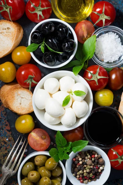 mozzarella, ingredients for the salad and bread on dark background, top view vertical