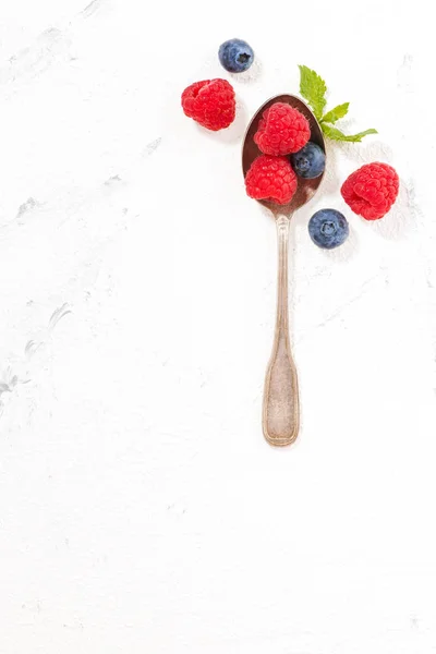 Spoon with berries and white background, top view