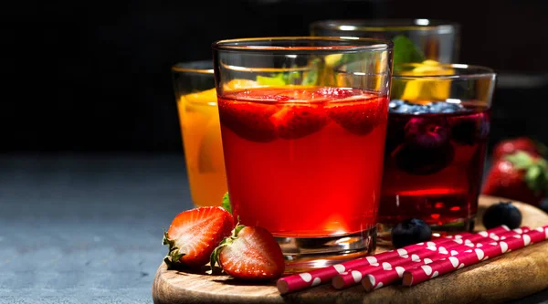 fruit and berry beverages in assortment on dark background, horizontal