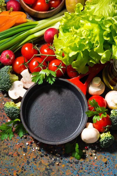 Empty cast iron skillet and fresh organic vegetables, vertical, — Stock Photo, Image
