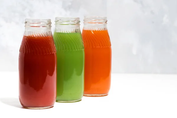 Kleurrijke groentesappen in flessen op witte tafel — Stockfoto