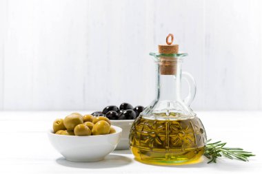 şişe zeytinyağı ve zeytin beyaz masa üzerinde kaseler ile