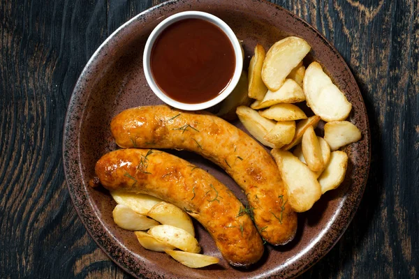 Fried pork sausages with potatoes and ketchup, top view, closeup — Stock Photo, Image