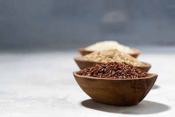Tres tipos de arroz seco en cuencos de madera, enfoque selectivo — Foto de Stock
