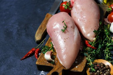 çiğ tavuk göğsü, baharat ve taze kekik bir kesme tahtası üzerinde