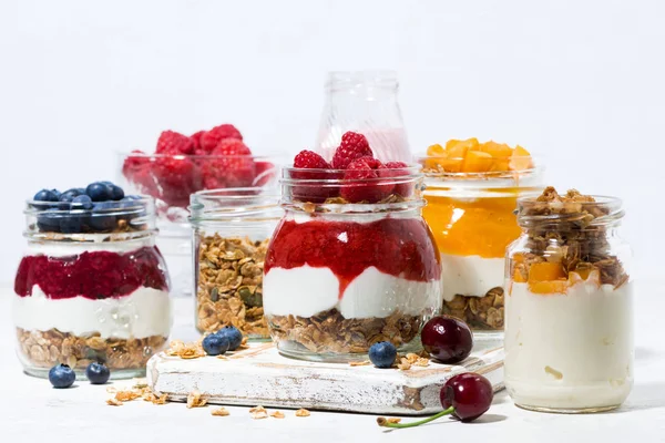 Десерты с мюсли, ягодами и фруктами в банках на белом столе — стоковое фото