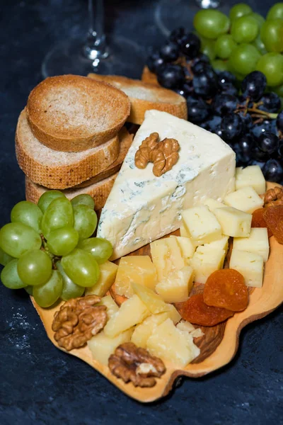 cheese platter on a wooden board, bread and fruit, vertical