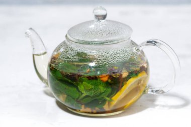 Beyaz arka planda cam çaydanlıkta taze naneli ve limonlu çay.