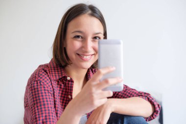 Genç kadın kameraya bakarak onun cep telefonuna internet tarama